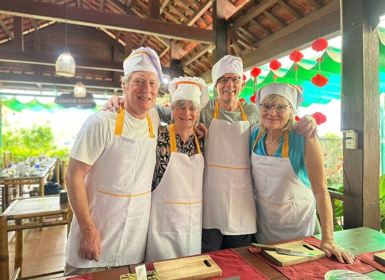 Four people wearing white aprons and chef hats standing in a covered outdoor area with tables and cutting boards. 5