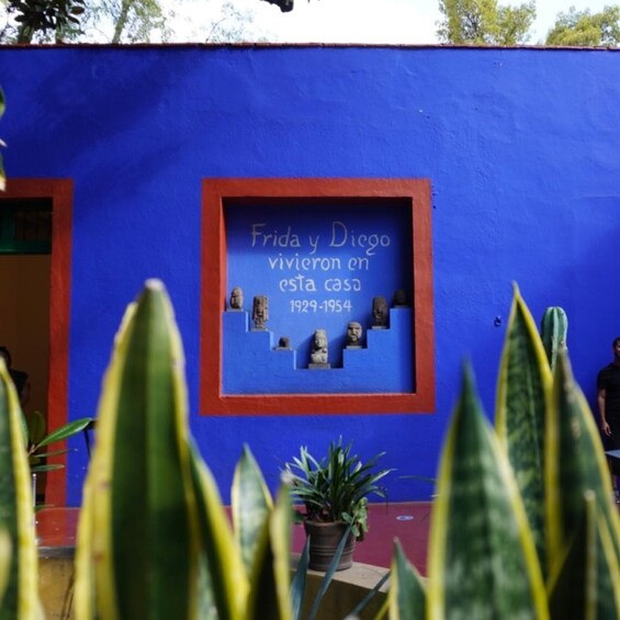 A blue wall with a plaque that reads "Frida y Diego vivieron en esta casa 1929-1954" and includes busts. 1