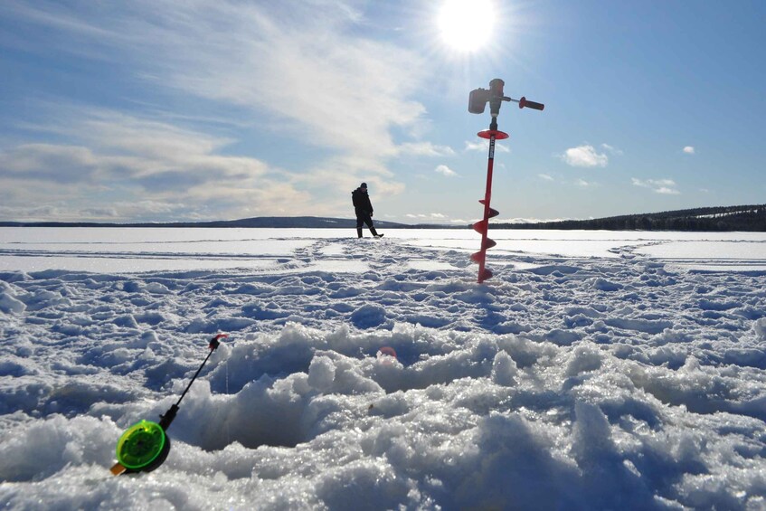 A snowy landscape with a person walking in the distance and a fishing rod in the foreground. 5