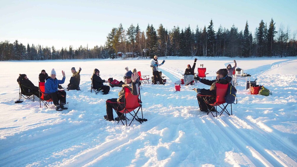 A group of people sitting on chairs in a snowy field with trees in the background. 1
