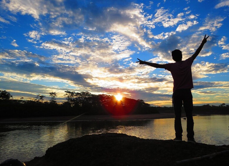 A person standing with arms raised, silhouetted against a sunset over a body of water. 5