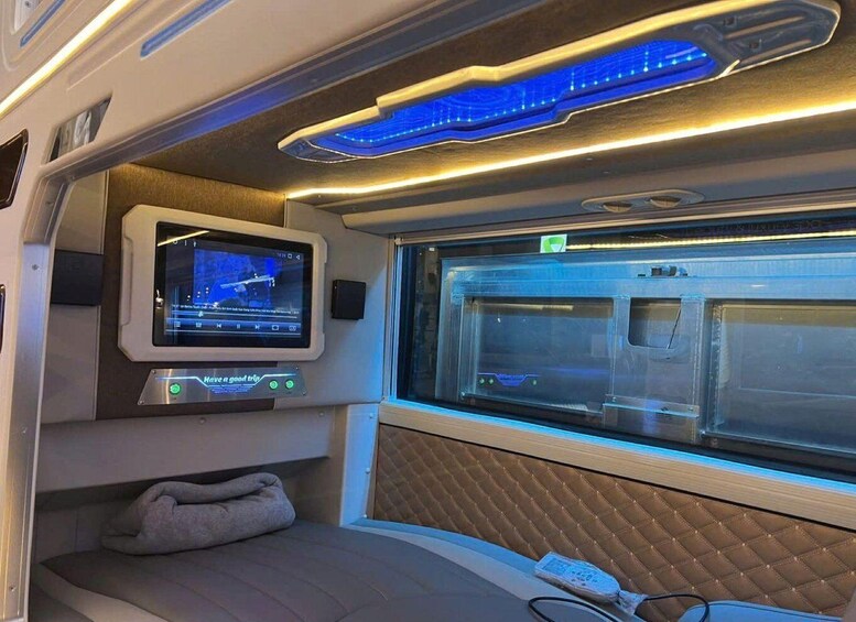 A train interior with a digital screen, a massage chair, and a window with a view of the outside. 2
