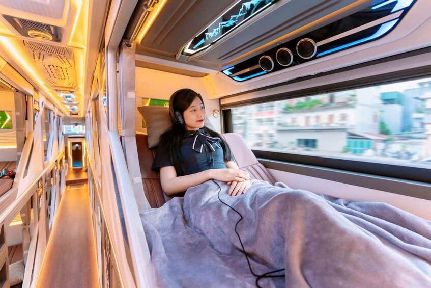 A person sitting in a train carriage with a blanket, windows, and interior lighting. 4