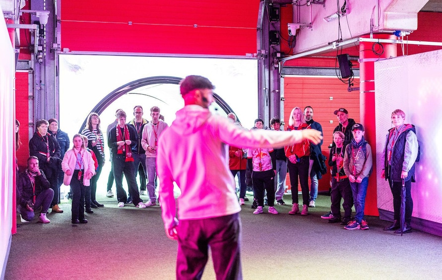 A group of people in a red industrial setting, some wearing lanyards and jackets, with a person in the foreground gesturing. 3