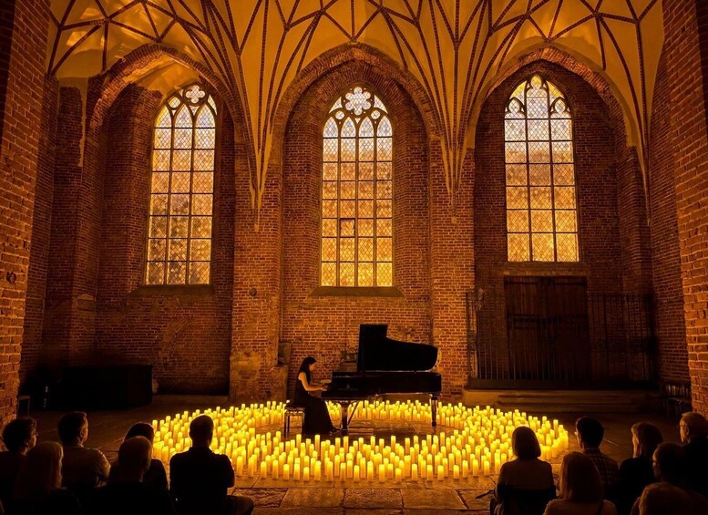 A grand hall with arched windows, a grand piano, and a circle of candles on the floor. 1