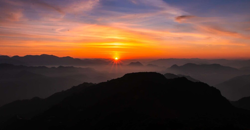A mountain range at sunrise with the sun visible between the peaks. 1