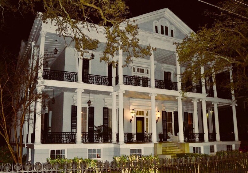 A large, white colonial-style building with multiple balconies and columns, illuminated at night. 3