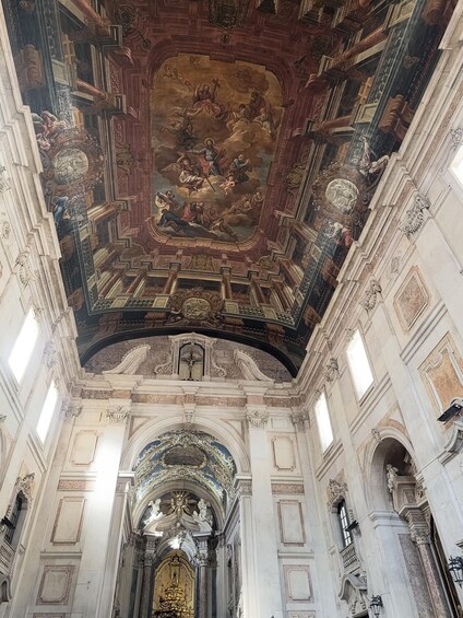 An ornate church interior with a detailed ceiling fresco, arched windows, and a central altar. 4