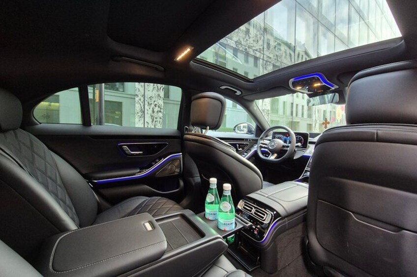 A luxury car interior with leather seats, a sunroof, and a center console with bottles. 4