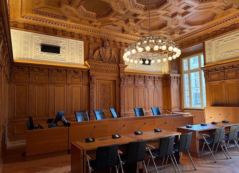 Een statige ruimte met versierde houten lambrisering, een grote kroonluchter en meerdere rijen stoelen. 5