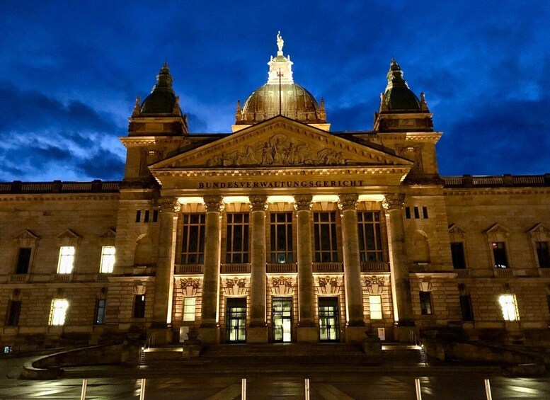 Een statig, verlicht gebouw met een grote koepel en twee kleinere koepels, met klassieke architectuur en zuilen. 4
