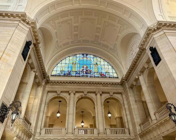 Een statig interieur met een groot glas-in-loodraam, gewelfde plafonds en klassieke zuilen. 2
