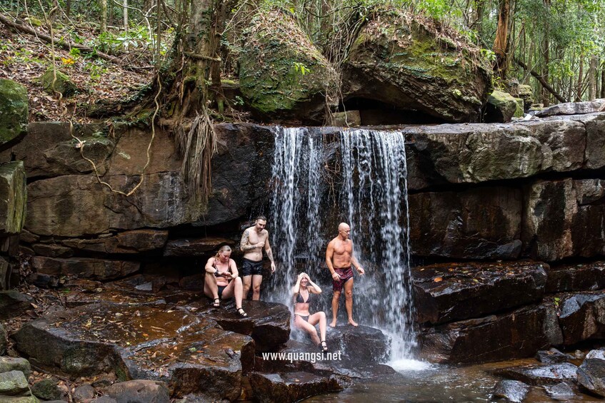 A waterfall in a forested area with people enjoying the water. 5