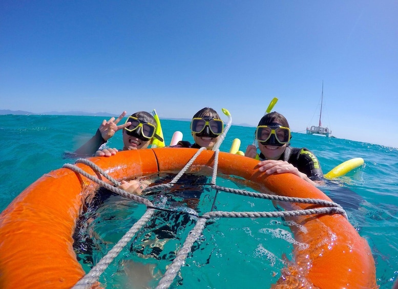 Three people snorkeling in clear blue water with an orange life ring and a boat in the background. 4