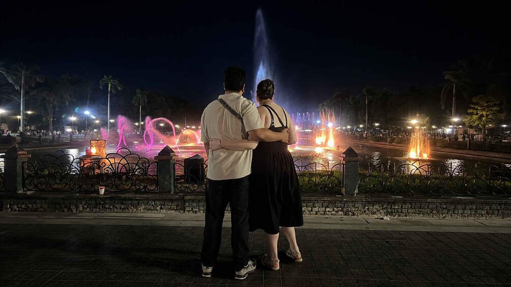 A couple standing in front of a fountain with colorful lights at night. 2