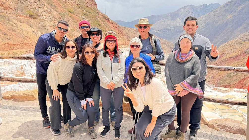 A group of people posing on a stone platform with a mountainous landscape in the background. 2