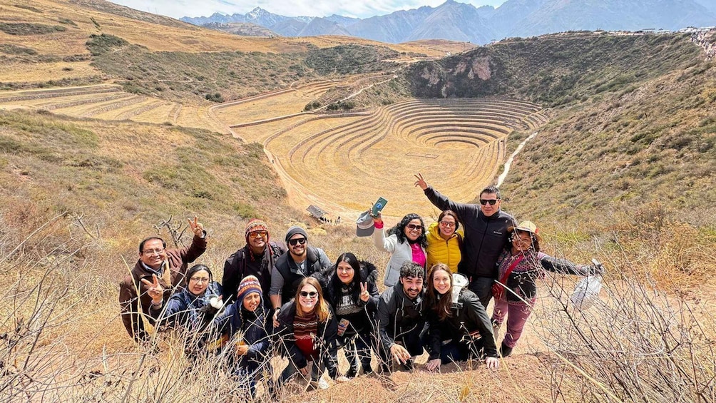 A group of people posing in front of a large spiral terraced structure in a mountainous landscape. 3