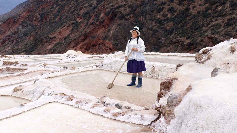 A person in traditional attire working in a salt flat with terraced pools. 5