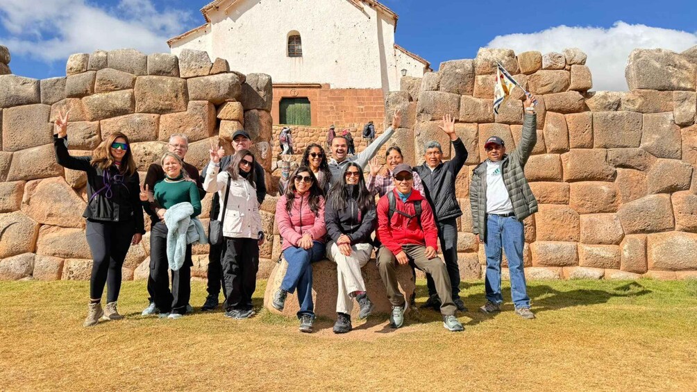 A group of people posing in front of a stone wall with a building in the background. 4