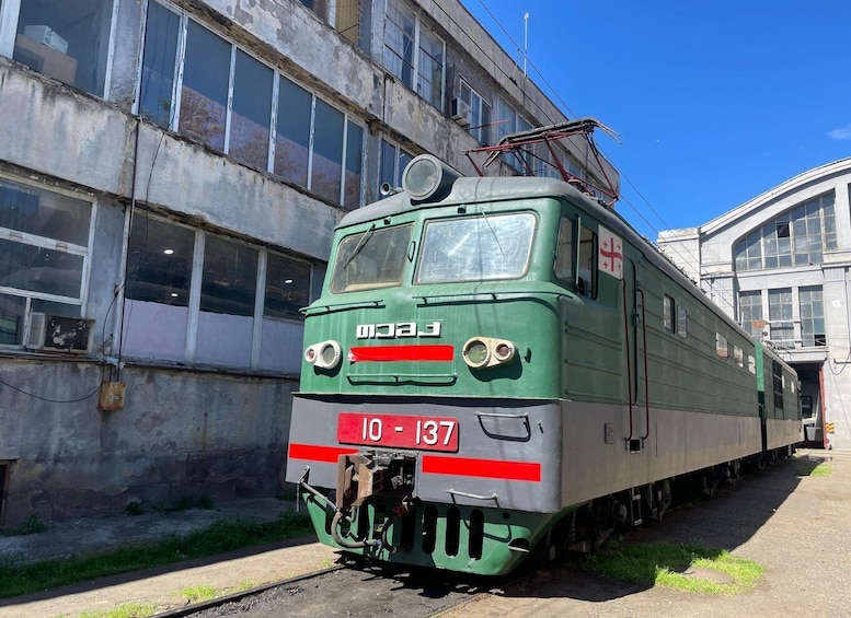 A green and white train with the number 10-137 parked next to a building. 1
