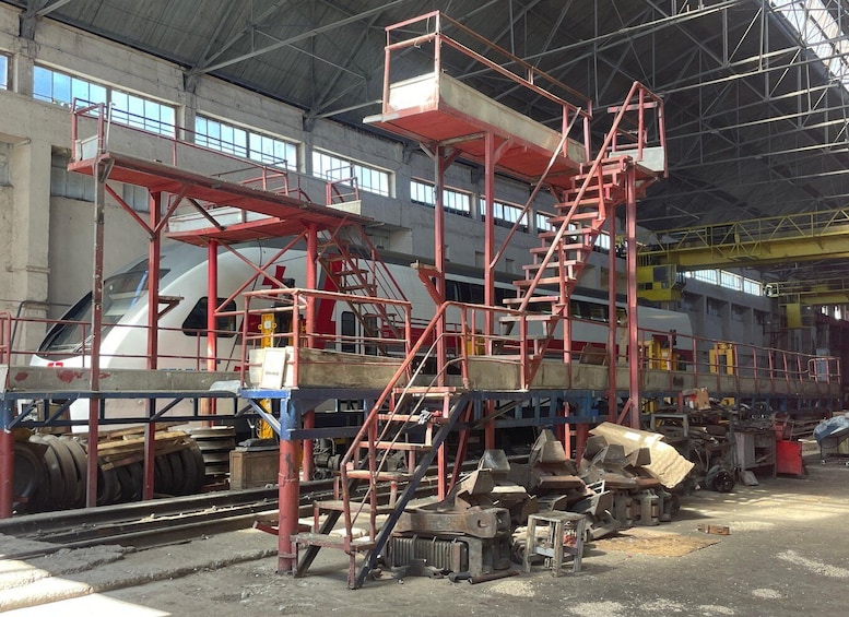 A train workshop with red scaffolding and various metal parts. 5