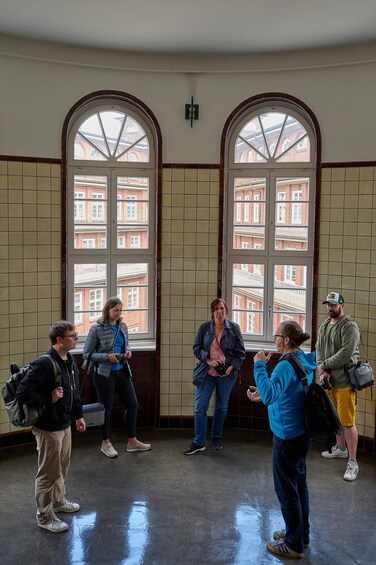 A group of people standing in a room with large arched windows overlooking a building. 3