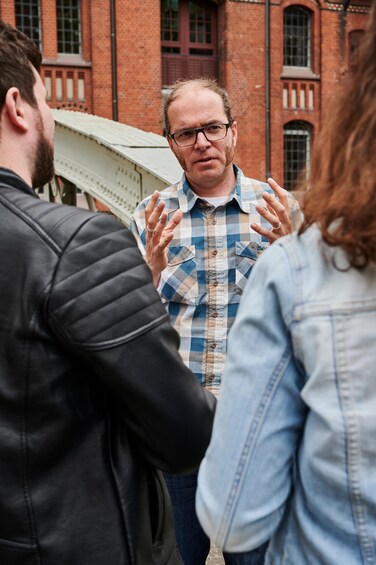 Three people standing outdoors in front of a brick building with large windows. 2