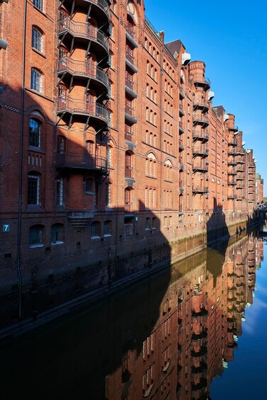 A red brick building with multiple balconies and a reflection in the water. 4