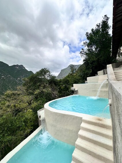 A swimming pool with a waterfall feature, surrounded by lush greenery and mountains in the background. 4