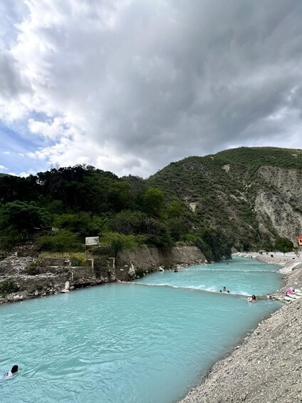A turquoise river with people swimming, surrounded by rocky cliffs and dense greenery. 5