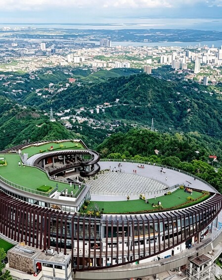 A modern amphitheater with a circular design, surrounded by lush greenery and a cityscape in the background. 5