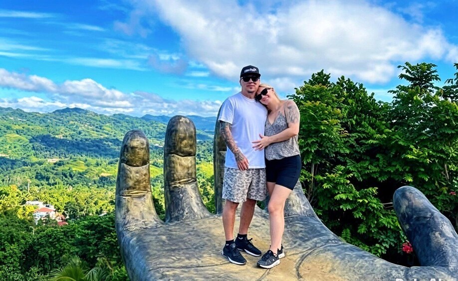 A couple standing on a large stone handprint with a mountainous landscape in the background. 1