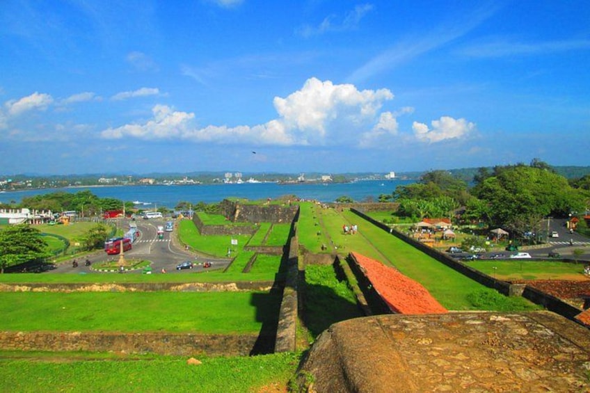 A coastal fortification with a clear view of the ocean, a road with vehicles, and a green landscape. 1