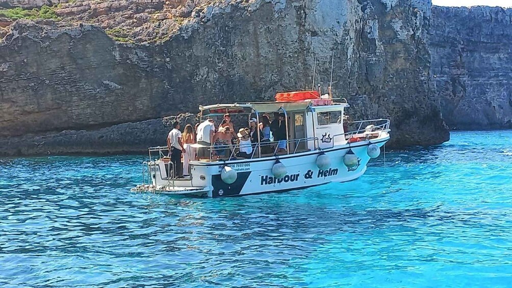 A boat named 'Harbour & Helm' on clear blue water with rocky cliffs in the background. 5