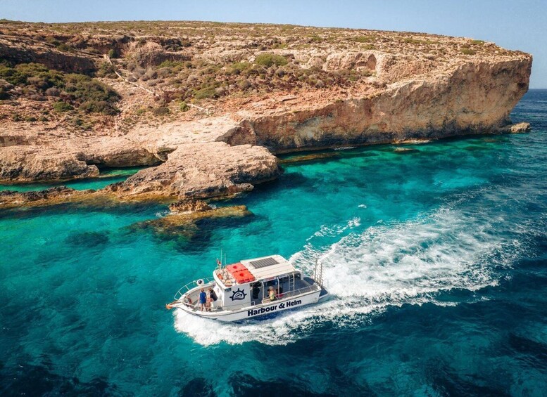 A boat named 'Harbour & Helm' navigating clear turquoise waters near rocky cliffs. 1