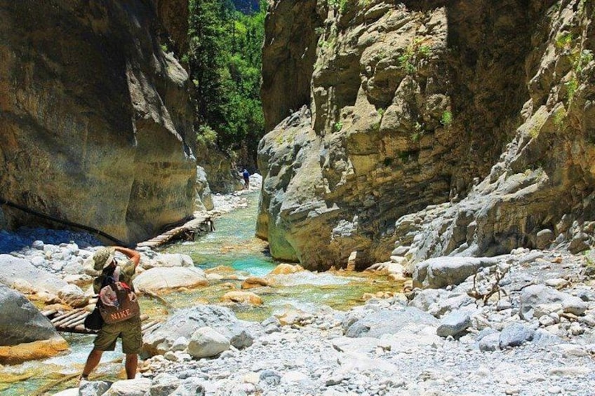 A rocky canyon with a clear stream, a person taking a photo, and a backpack. 5