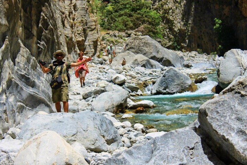 A rocky riverbed with large boulders and a person pointing at something. 1