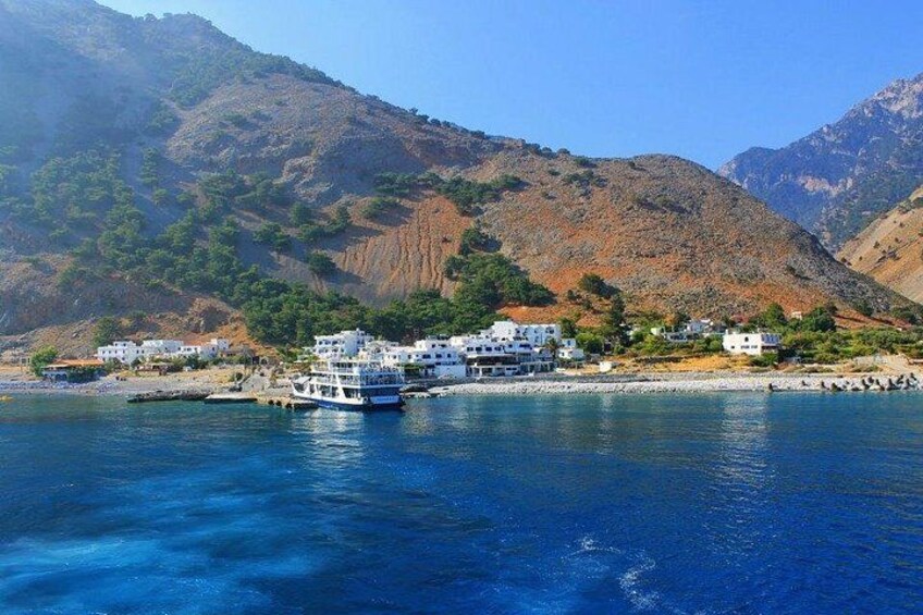 A coastal town with white buildings, a boat docked at the pier, and mountains in the background. 2