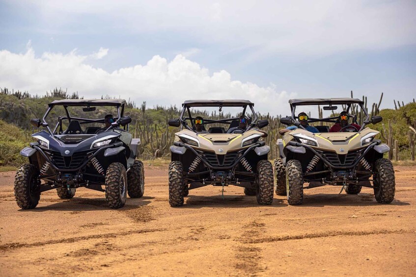 Three off-road vehicles parked on a dirt road with a natural landscape in the background. 1