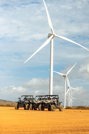 Two off-road vehicles parked in a desert with wind turbines in the background. 5