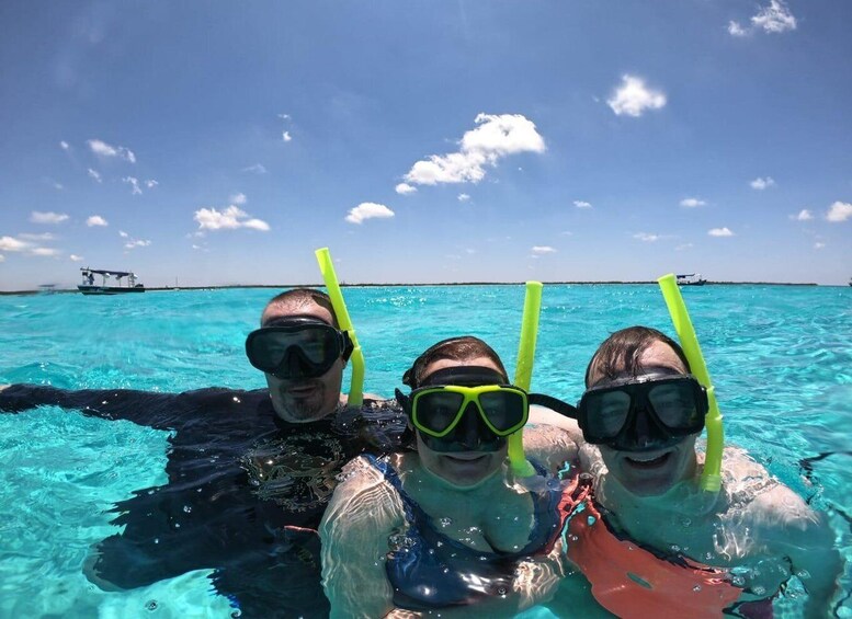 Three people snorkeling in clear blue water with a boat and a ship in the background. 4