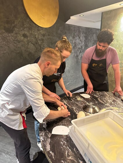 Three people working with dough on a marble countertop in a kitchen. 1