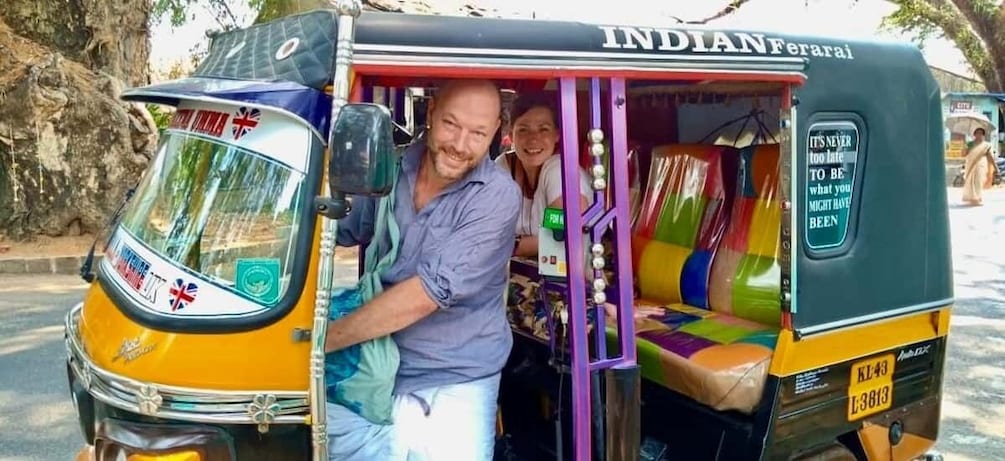 An Indian auto-rickshaw with colorful interior and a man sitting in the driver's seat. 3