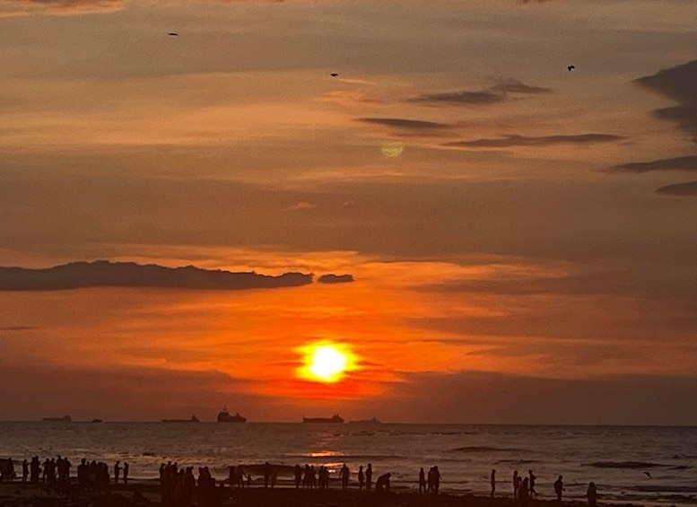 A sunset over the ocean with silhouettes of people on the beach and ships in the distance. 5