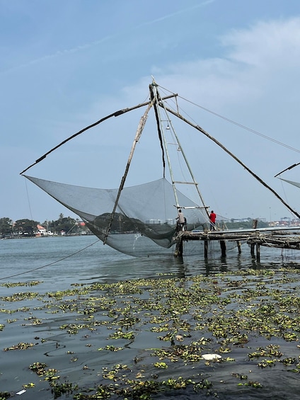 A traditional fishing net structure over water with people standing on stilts. 2