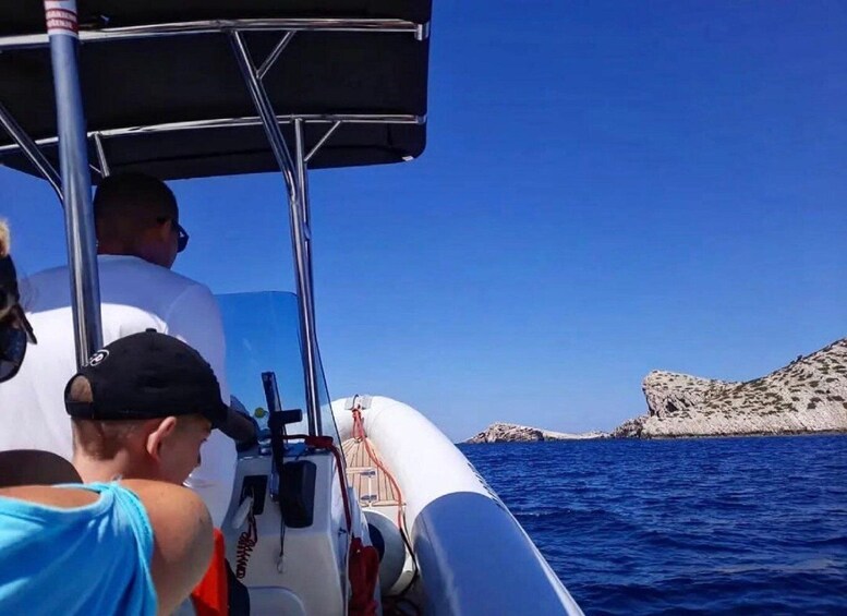 A boat with people on board, a rocky coastline, and clear blue water. 3