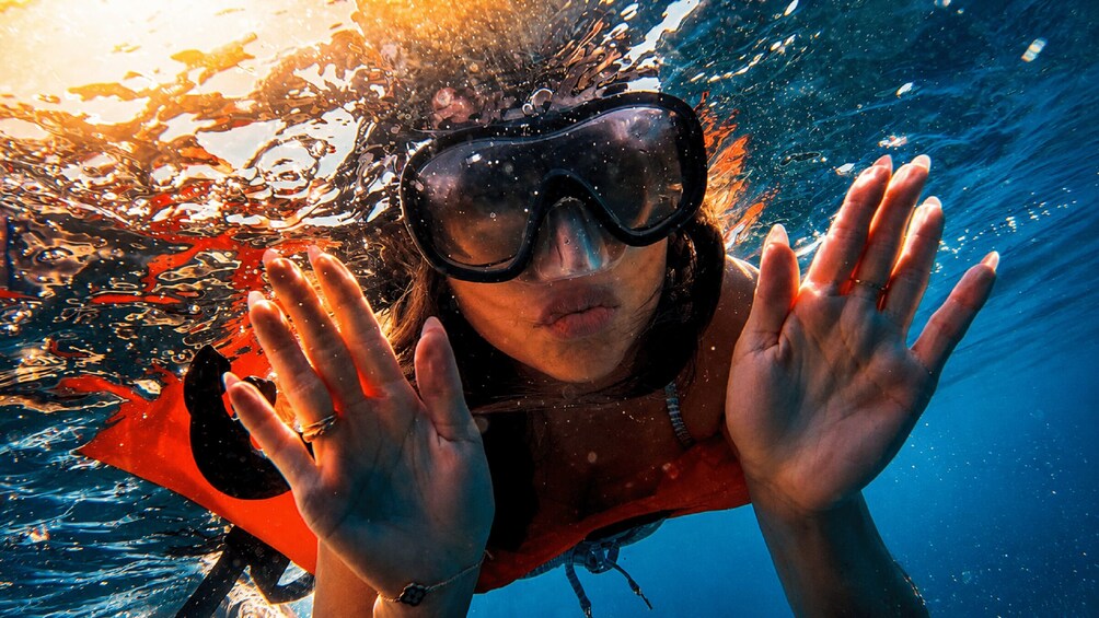 A person underwater with a red and black wetsuit, wearing goggles, and holding their hands up. 2