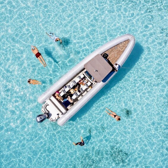 An inflatable boat on clear blue water with people swimming around it. 1