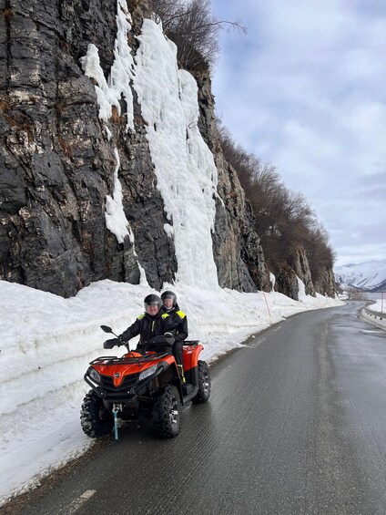A snow-covered road with a rocky cliff on one side and a mountain in the distance. 1