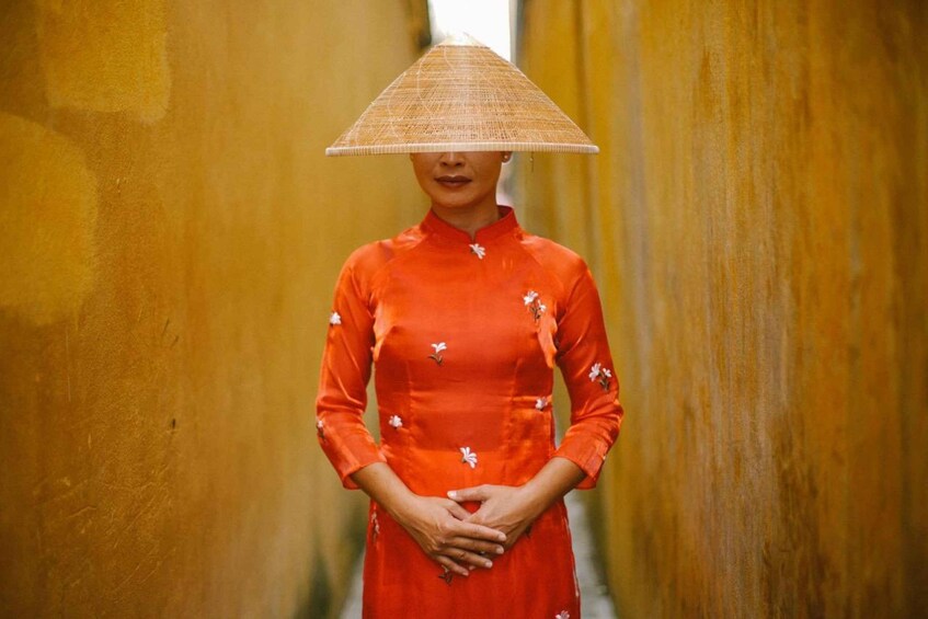 A person in a red dress with floral patterns standing in a narrow alleyway. 1